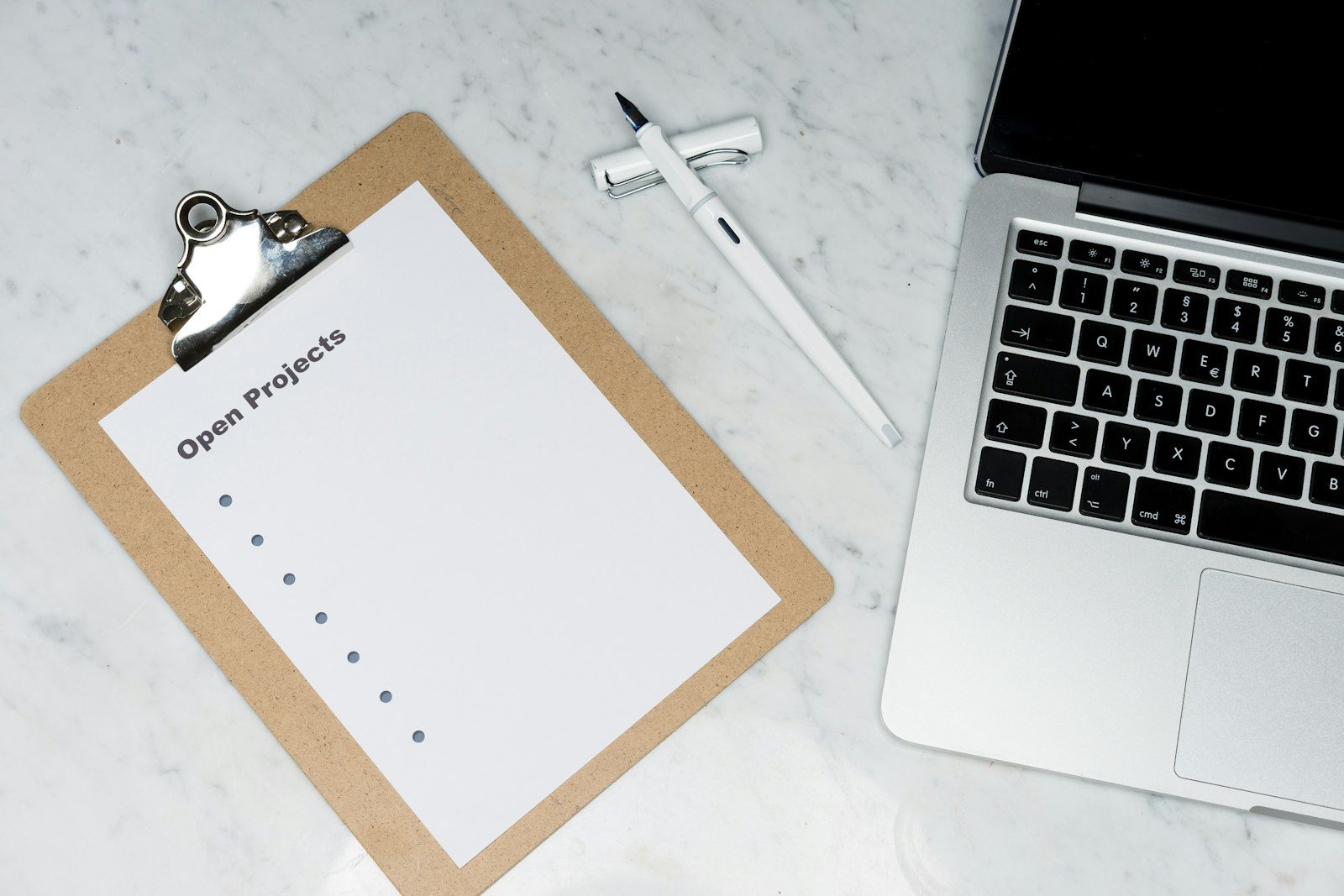 A clipboard with a project checklist next to an open laptop on a marble desk
