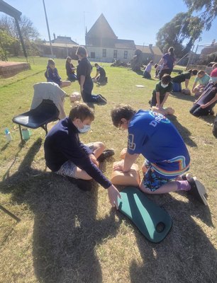 Participants practising CPR compressions on training manikins outdoors during a REACHAU first aid course