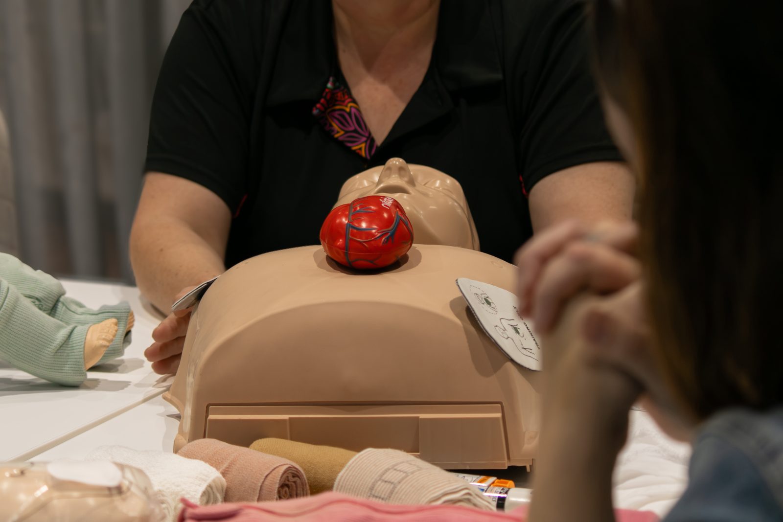 First aid trainer with a CPR manikin guiding a student through refresher practice