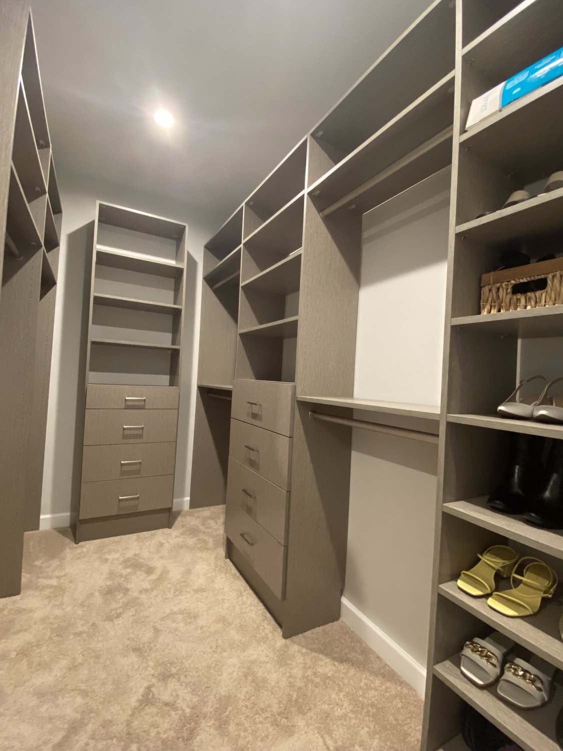 Greige walk-in closet with a drawer tower, open shelving and shoe shelves running floor to ceiling