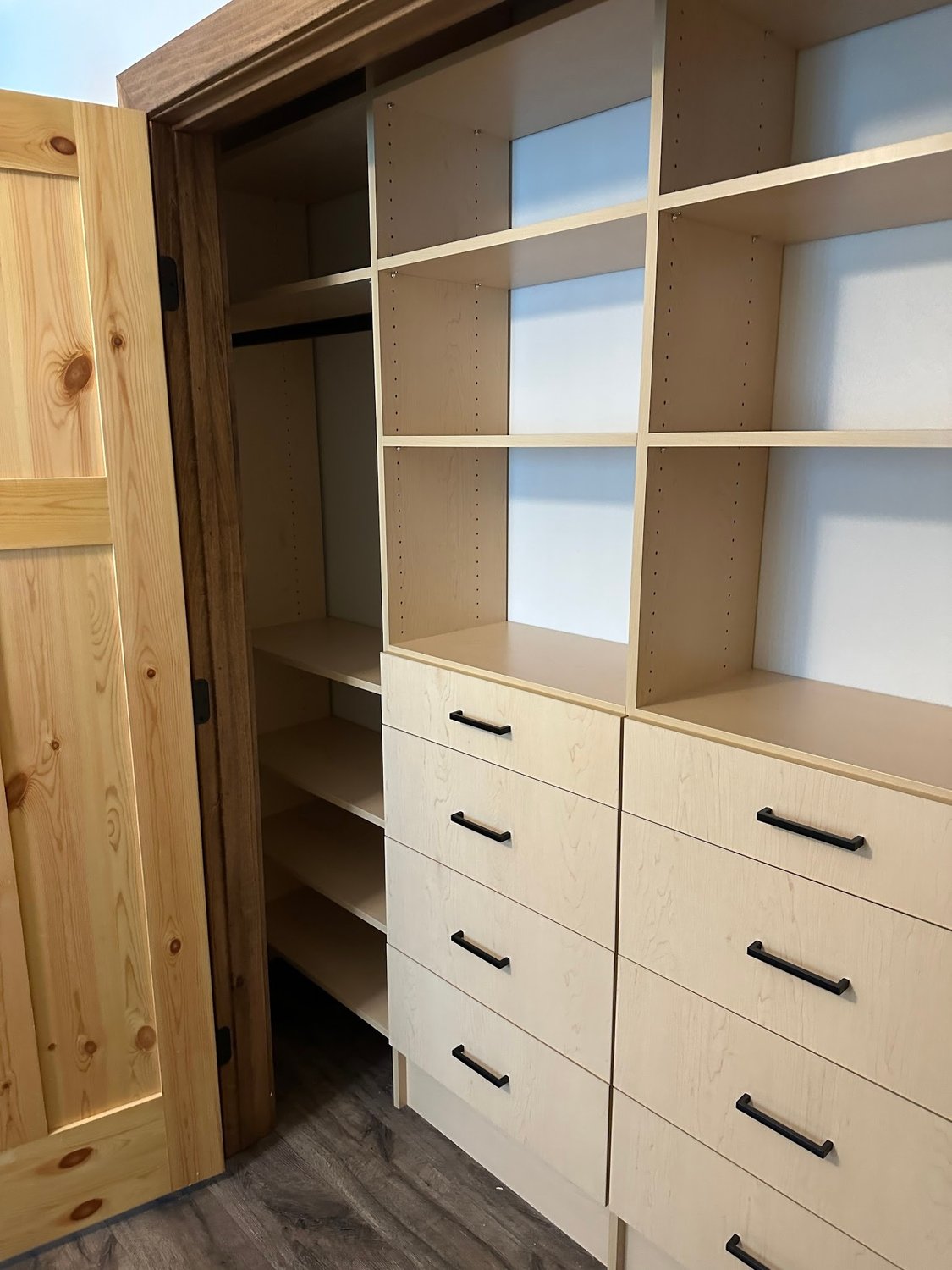 Reach-in closet with cream shelving and a drawer stack behind open wood doors