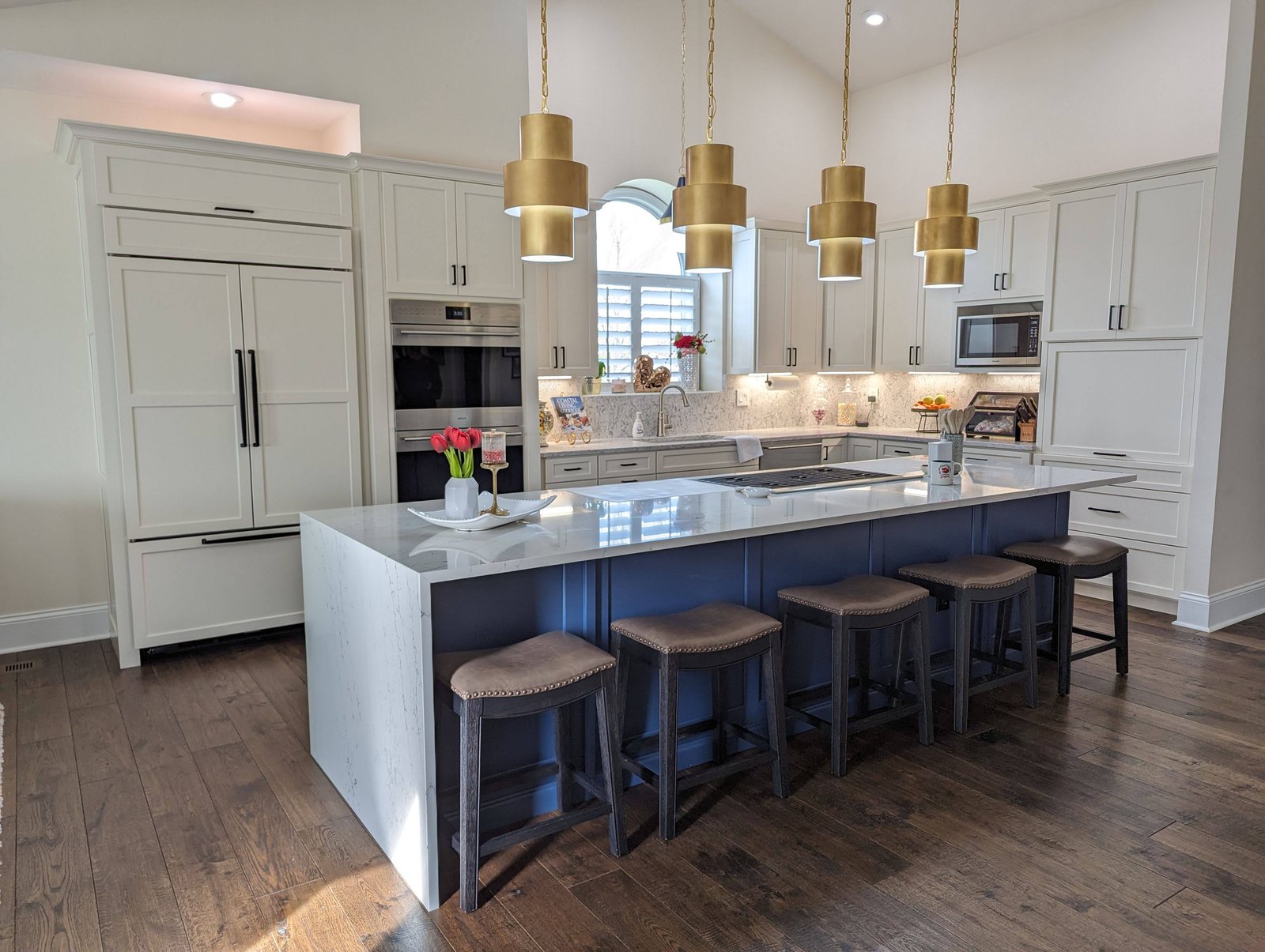 Updated kitchen with white cabinetry, a navy island and brass pendant lights