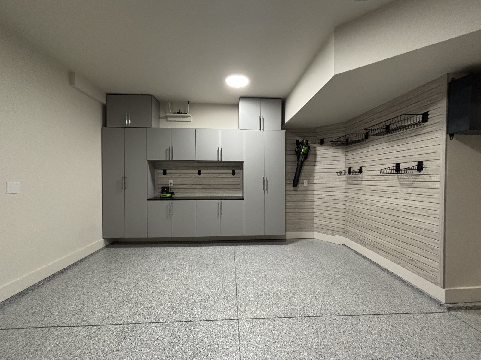 Garage with gray cabinets, slatwall storage and an epoxy floor