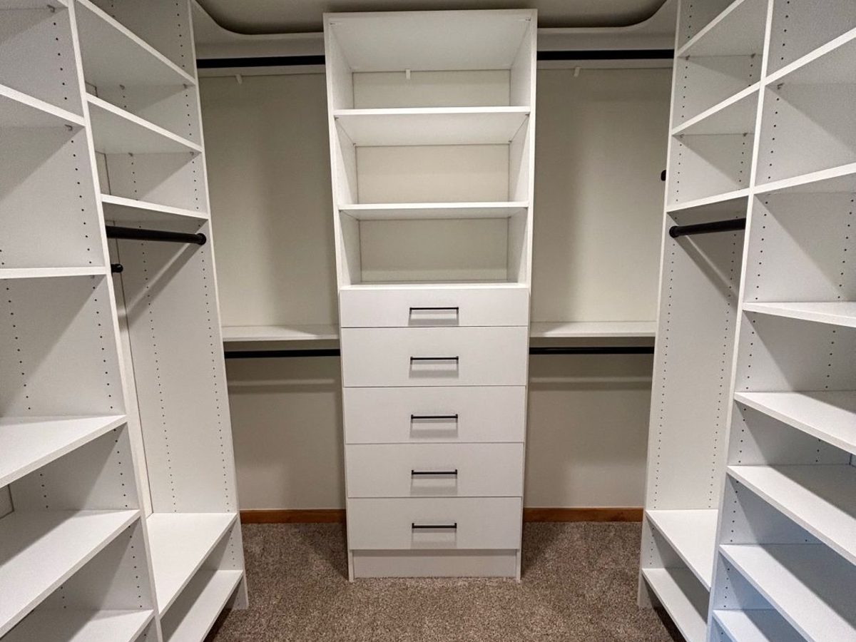 A white walk-in closet with a center drawer tower and adjustable shelving