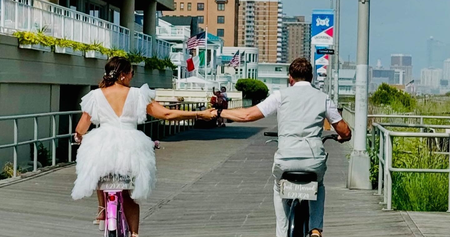 Newlyweds riding bikes hand in hand on the Ocean City boardwalk, Just Married signs on their bikes