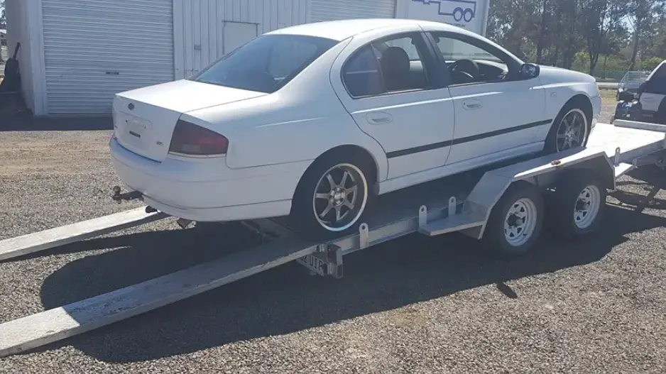 White sedan loaded on a tandem car trailer with pull-out ramps