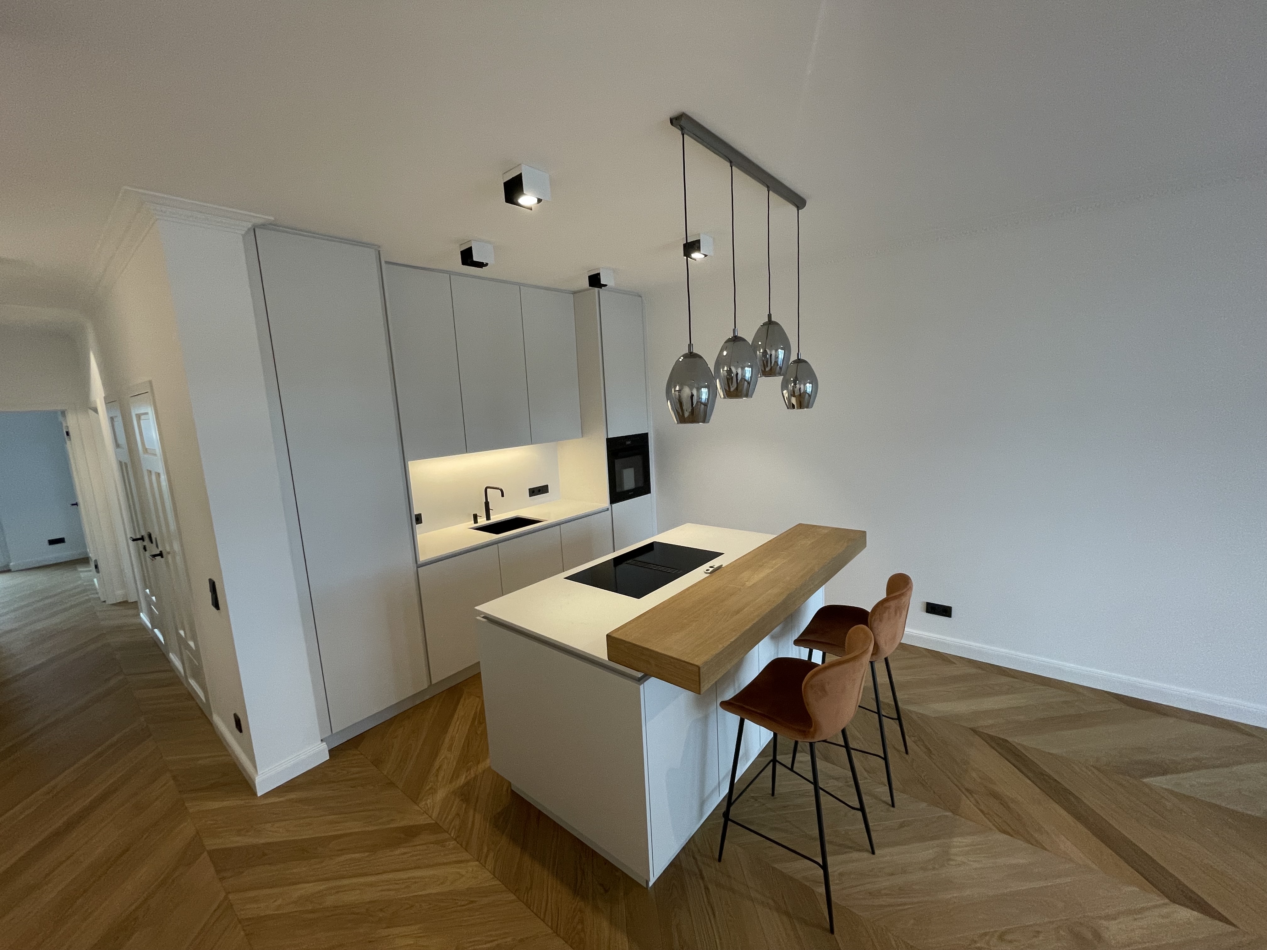 Moderne, weiße Küche mit Kochinsel, integrierter Holztheke und zwei braunen Barhockern.