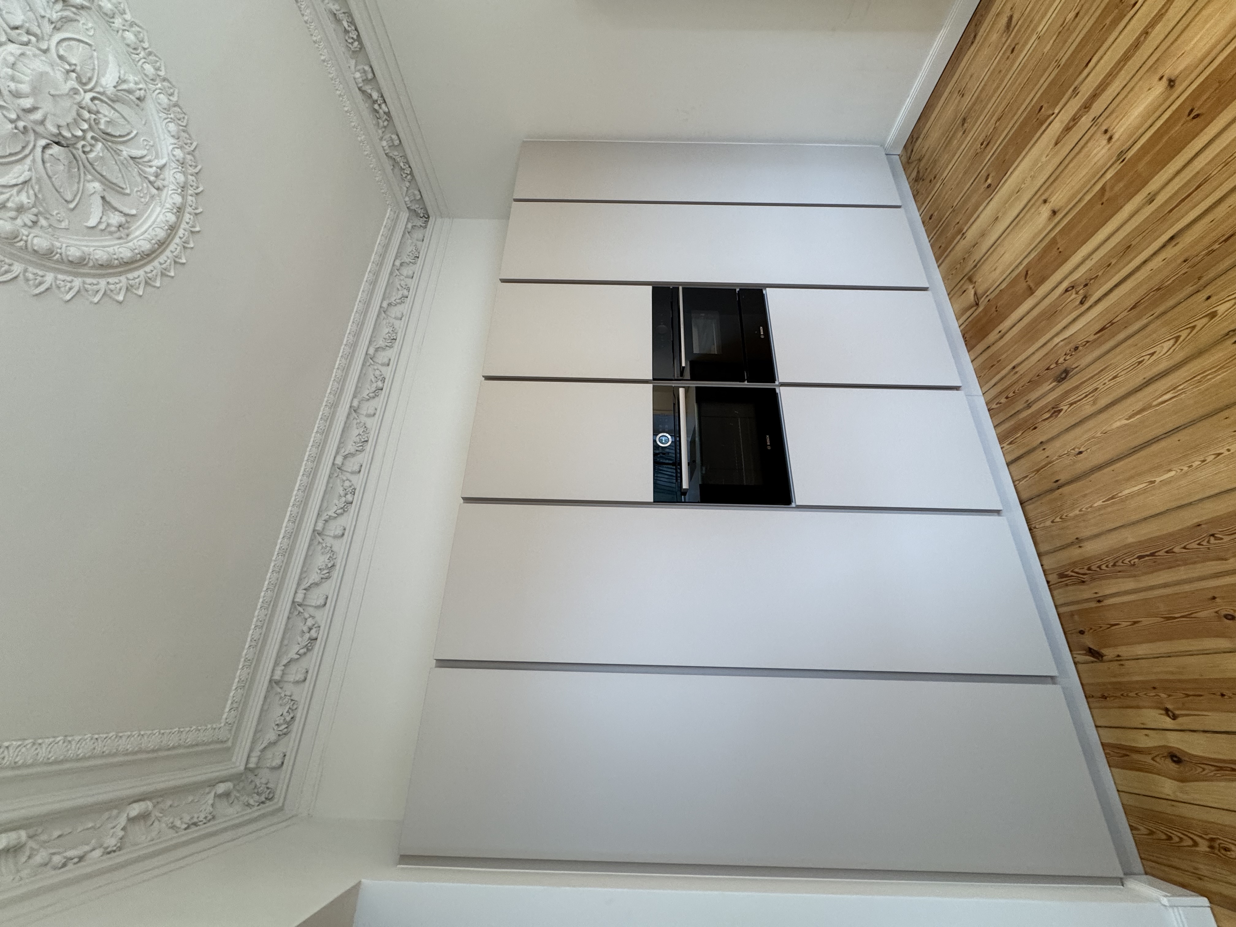 Weiße Einbauküche mit integrierten Elektrogeräten und Stuckrosette im Altbau