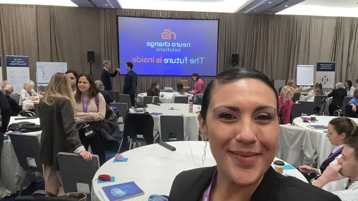 Suhey smiling at a professional conference, attendees at round tables behind her