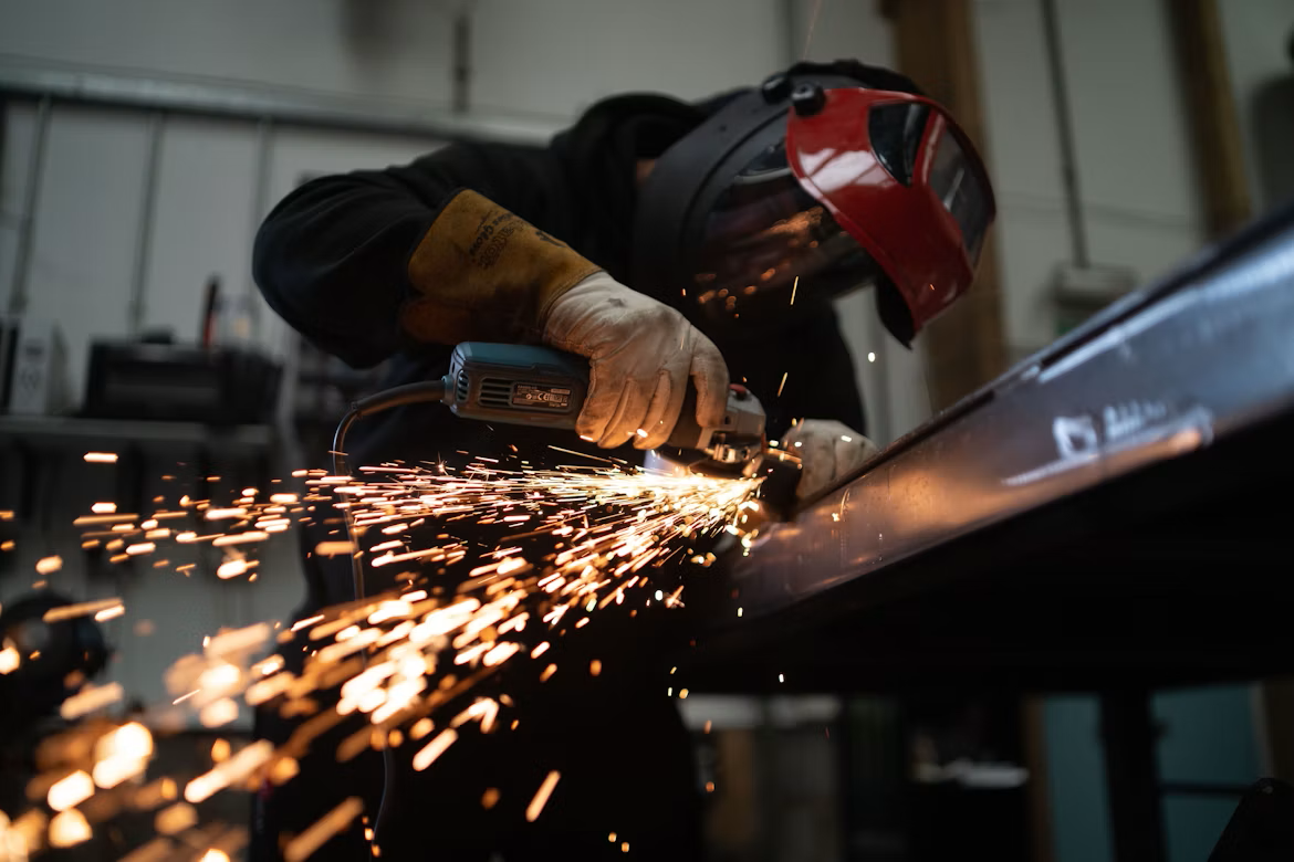 Metal fabrication worker grinding steel beam