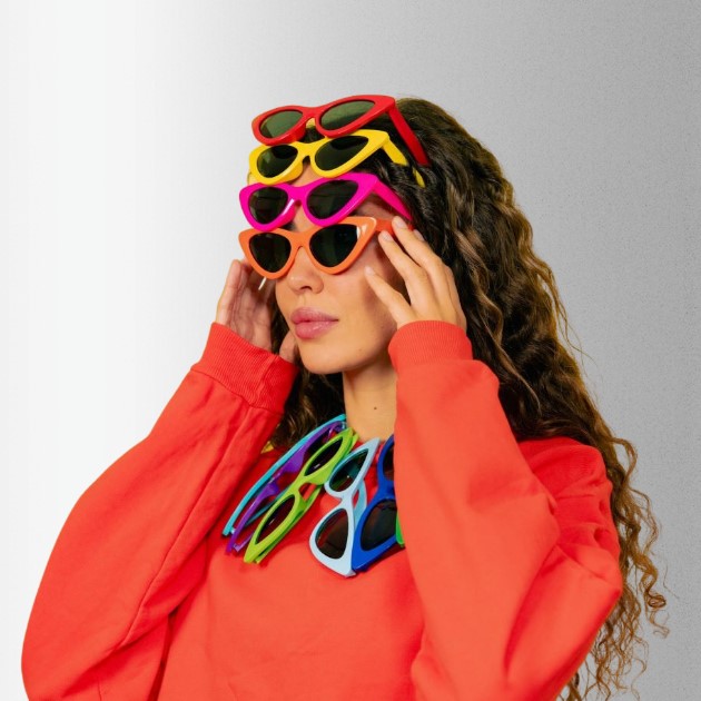 A woman in bright orange has different colors of sunglasses stacked up her forehead and tucked into her collar.
