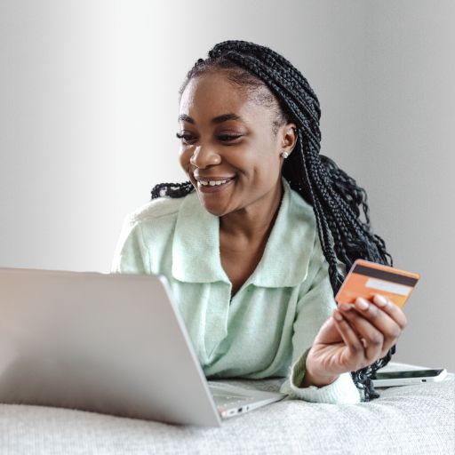 A woman smiles as she types on a laptop with one hand while holding a credit card with the other.