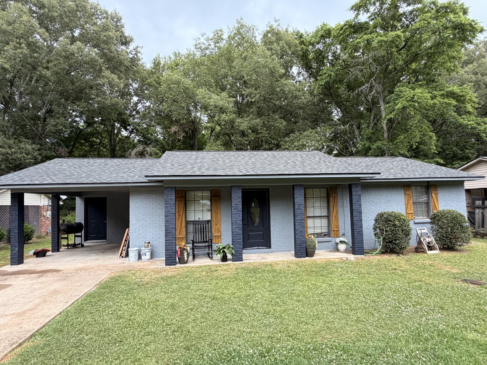 Single-story brick ranch home with brick painted light blue-gray, navy porch columns and front door, and wood-tone shutters