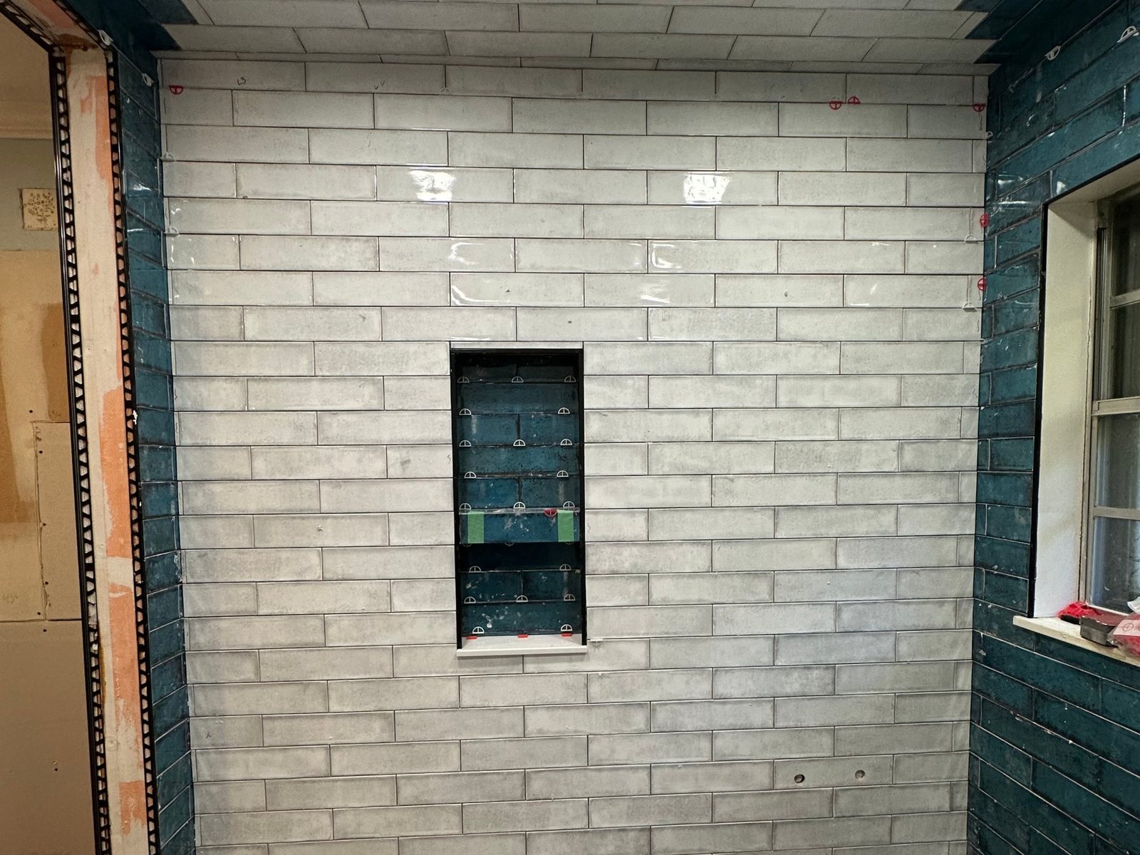 Tile shower remodel in progress with glossy white and blue elongated wall tile and a recessed tile-lined niche