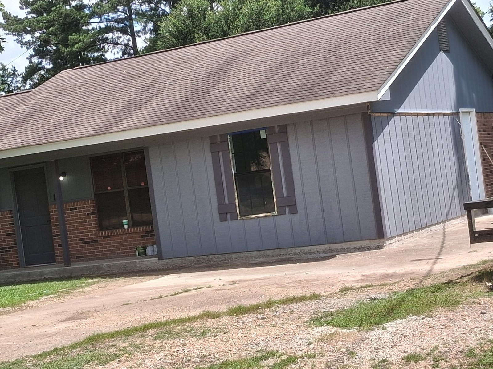 Home addition under construction with new gray vertical siding, a newly set window awaiting trim and dark shutters