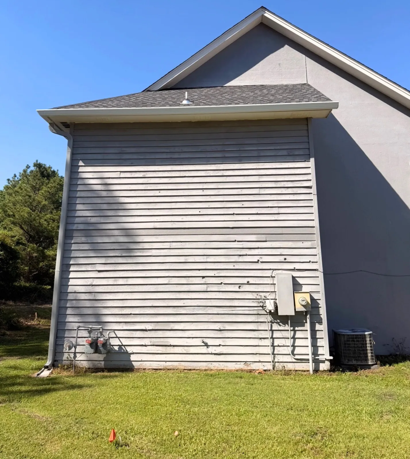Side wall of a two-story home covered in worn horizontal lap siding before stucco installation