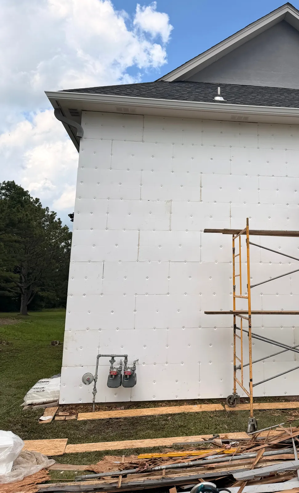 Side wall covered in white board panels with scaffolding set up for stucco installation