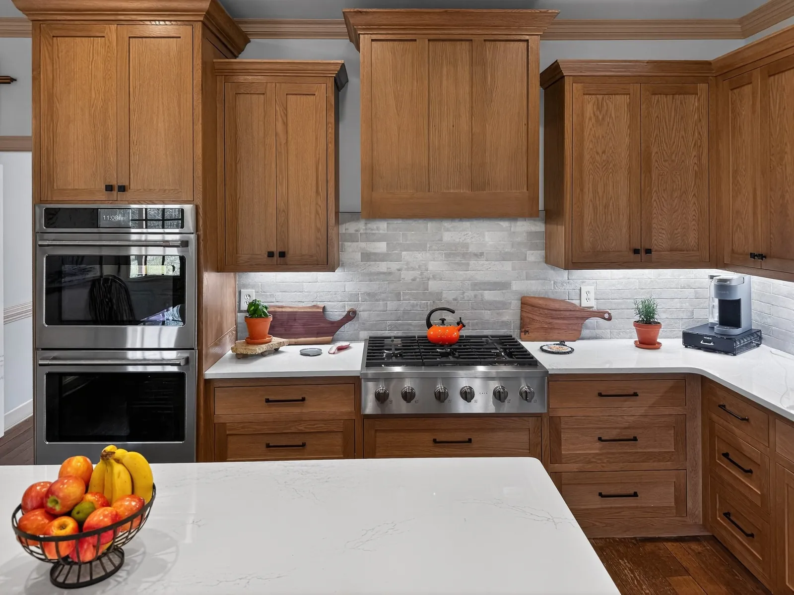 Double wall oven in a tall wood cabinet next to a gas rangetop and gray brick-look backsplash