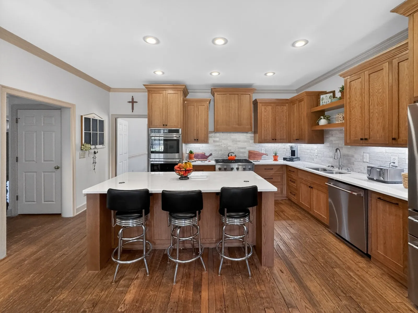 Kitchen island with a white countertop and three black bar stools facing the cabinet wall