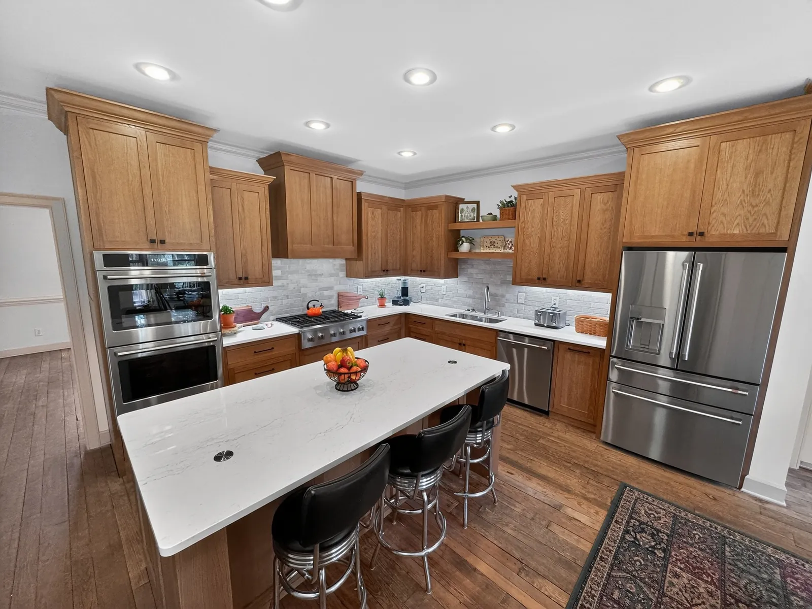 Finished kitchen with wood cabinets, stainless appliances and a white-topped island with three bar stools