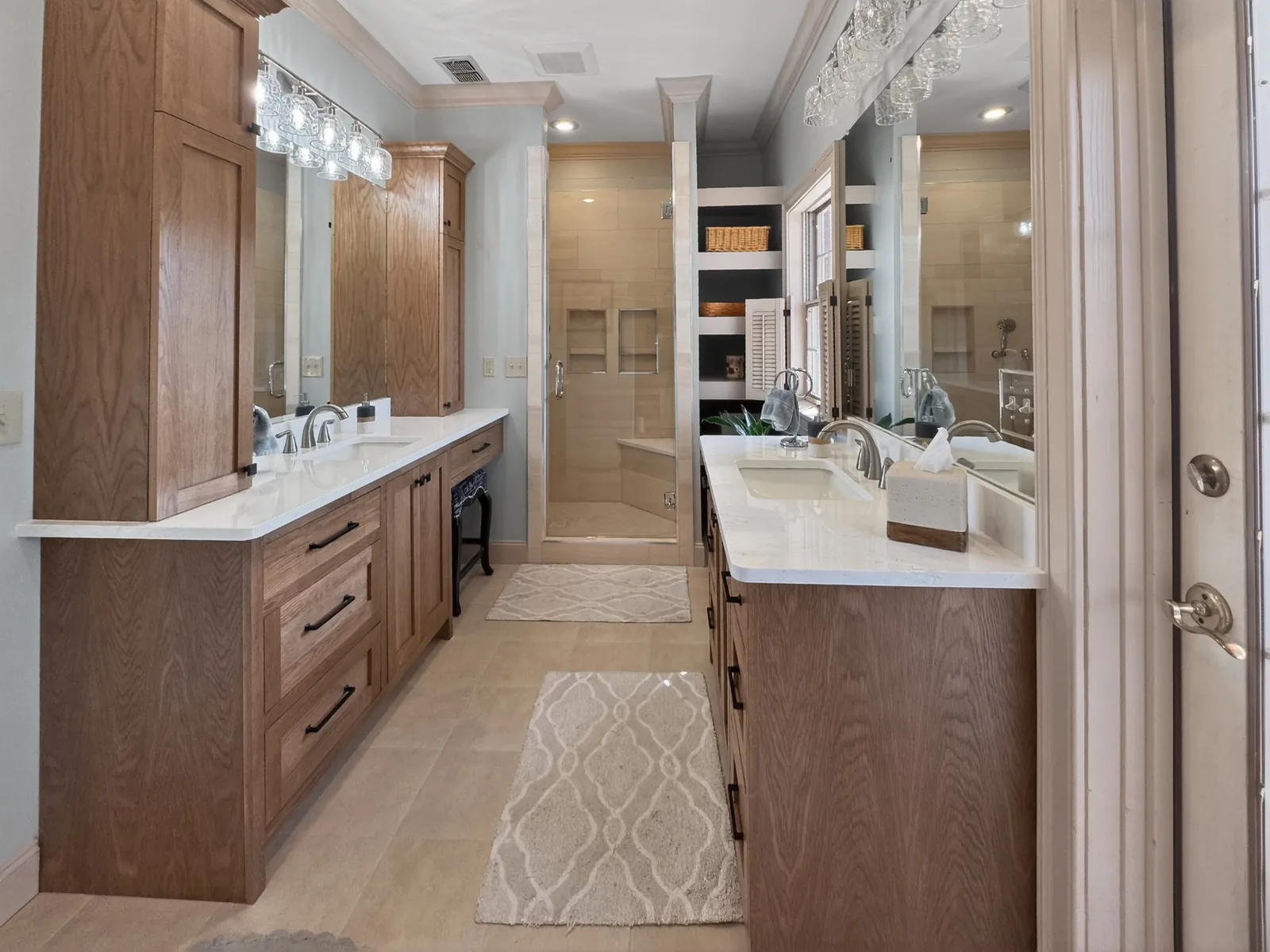 Two wood vanities with white countertops facing each other, with the walk-in shower at the far end of the bathroom