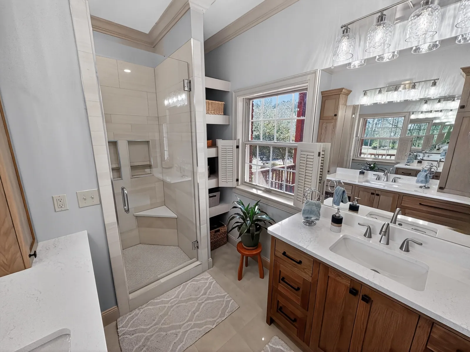 Glass-enclosed walk-in shower with light tile walls next to a wood vanity and window