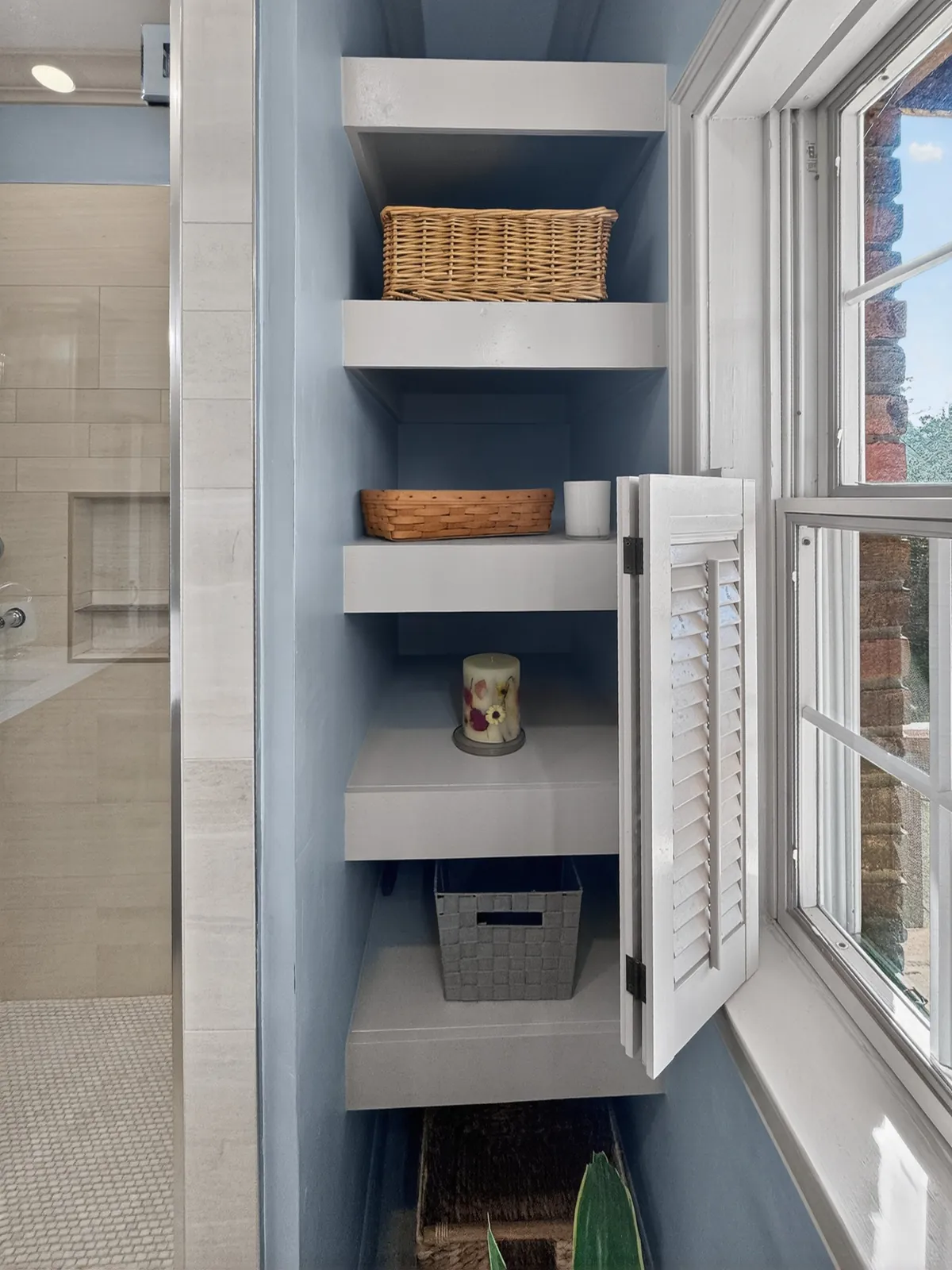 Painted built-in open shelves with baskets beside a bathroom window