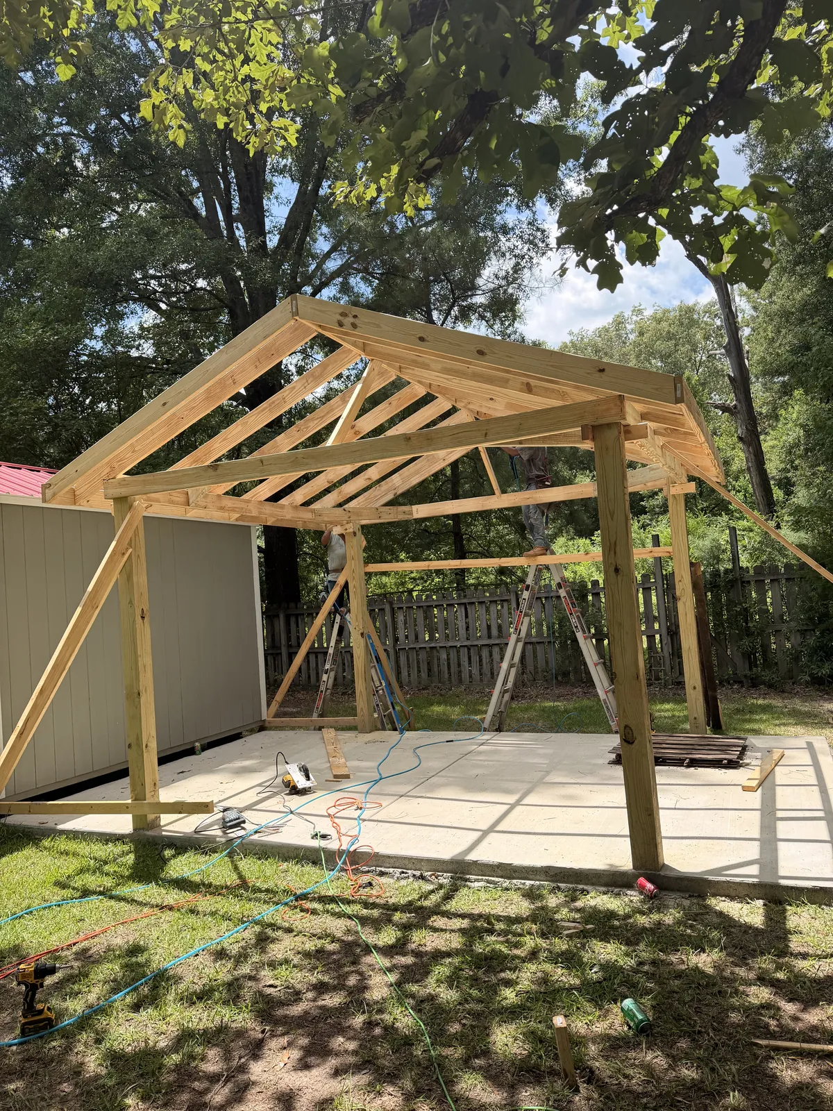 Timber carport frame with posts, beams and rafters on a new concrete pad, with a worker on a ladder