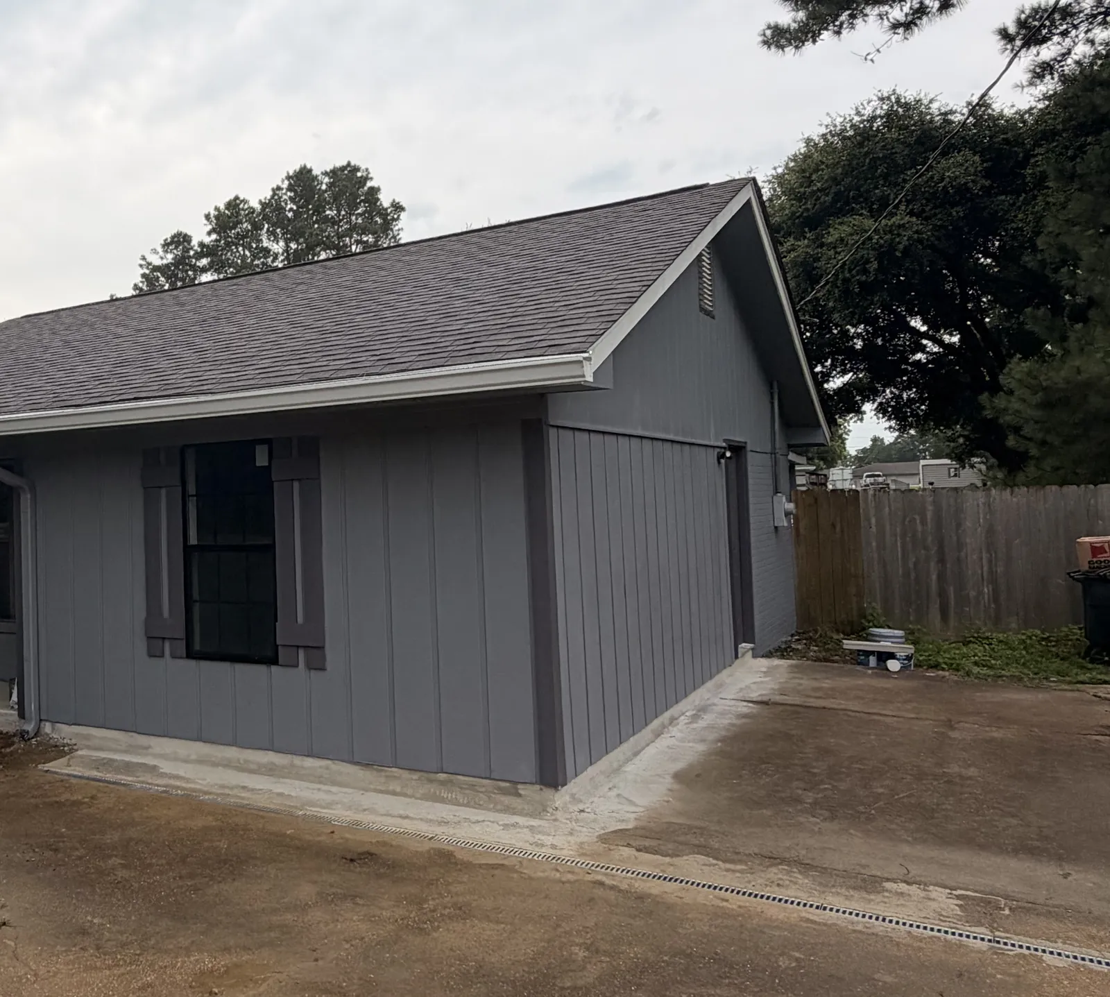 Side view of the finished home addition with gray vertical siding, a window with dark shutters and a side door