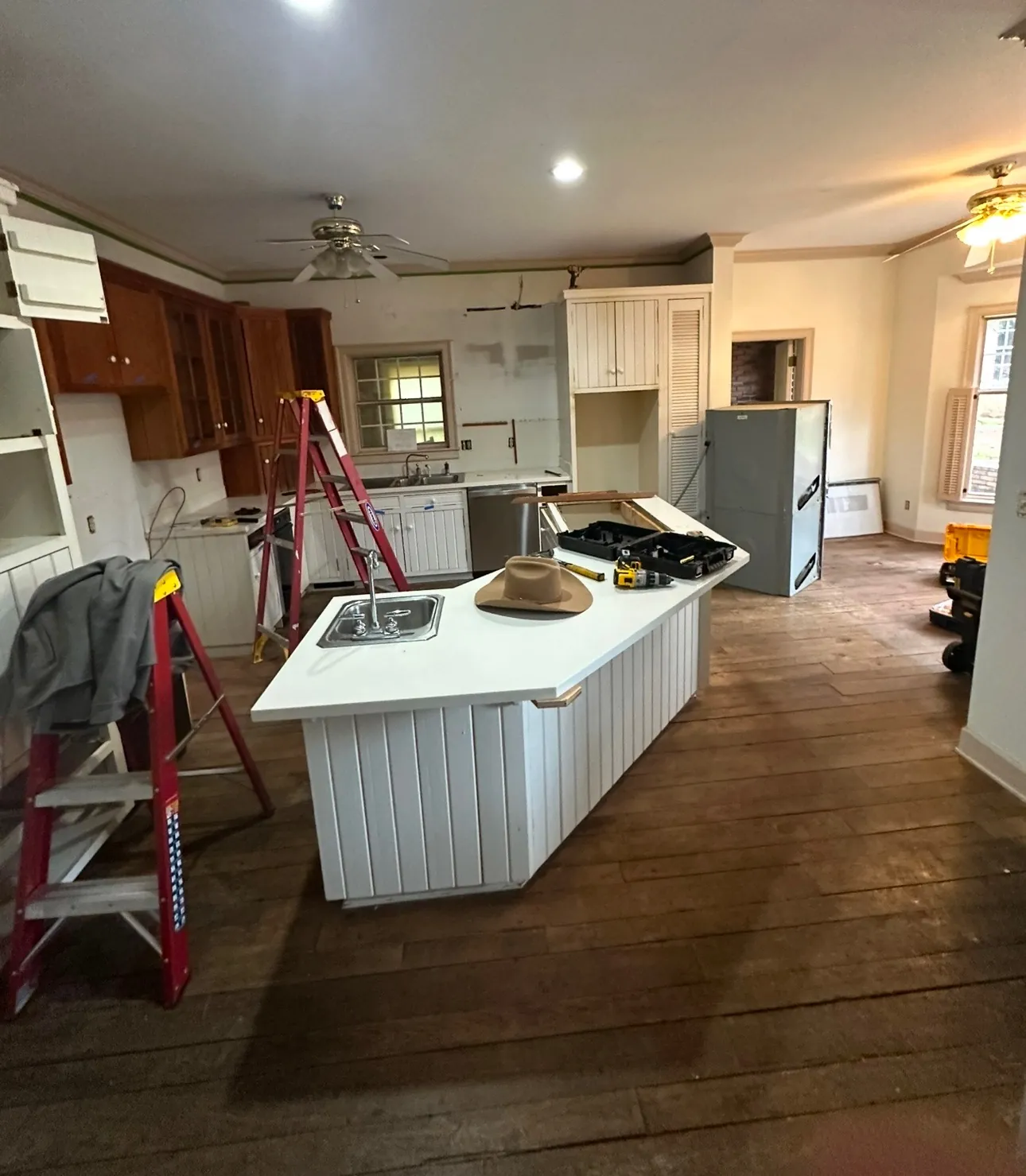 Original kitchen with white beadboard island and wood cabinets as demolition began, with ladders and tools in the room