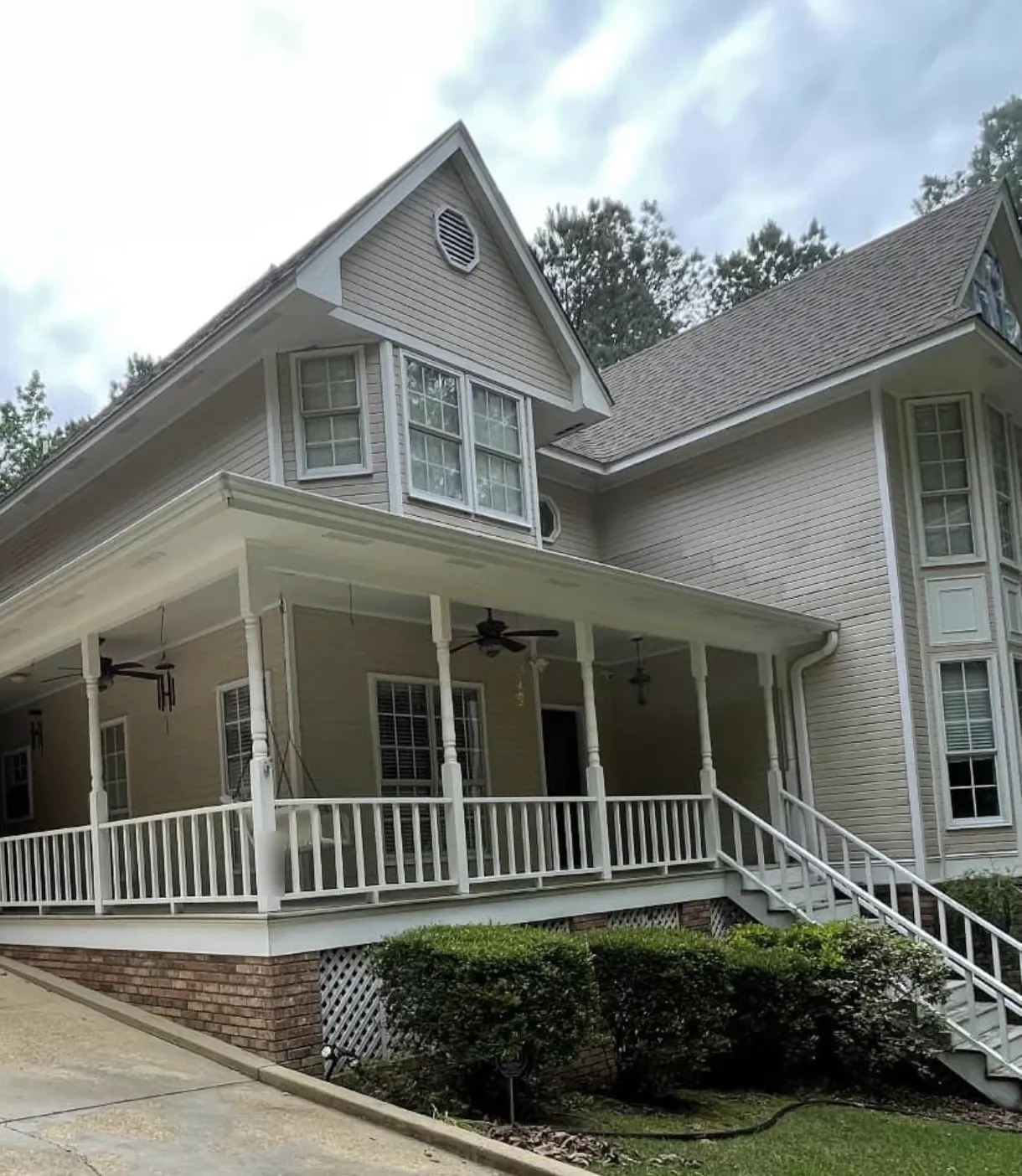 Two-story home with a wraparound porch and pale cream siding before exterior painting