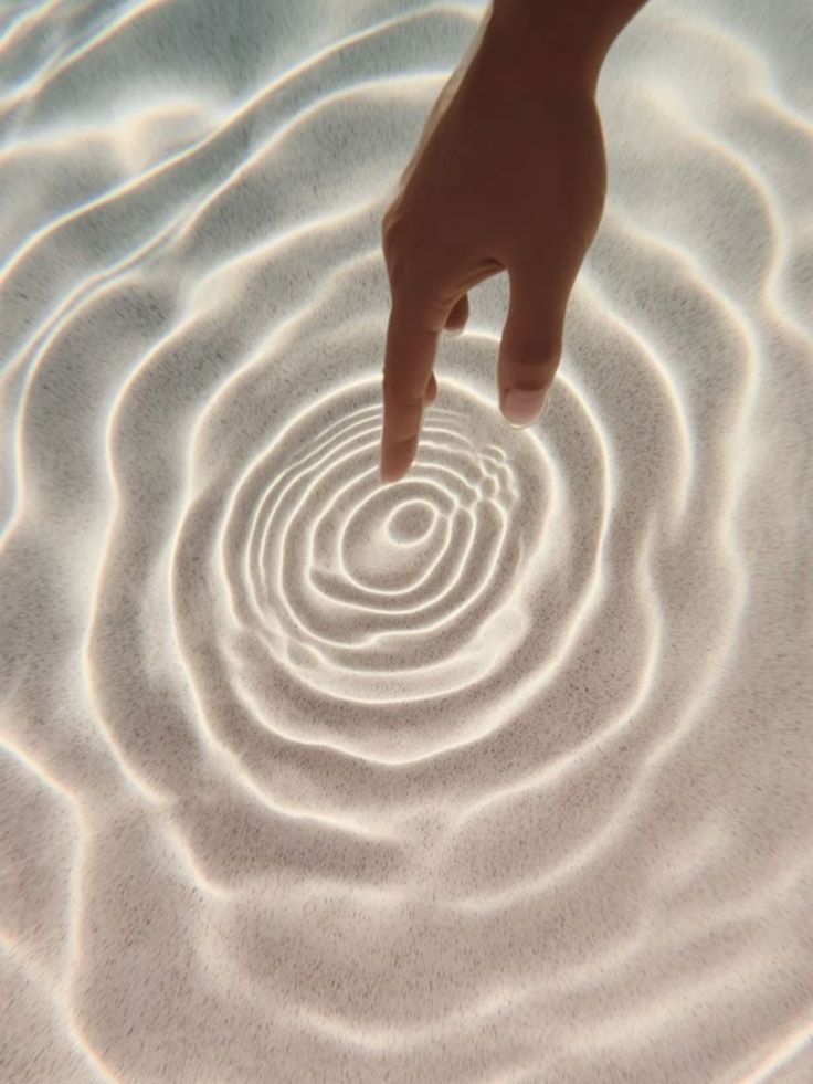 A fingertip creating ripples in shallow water