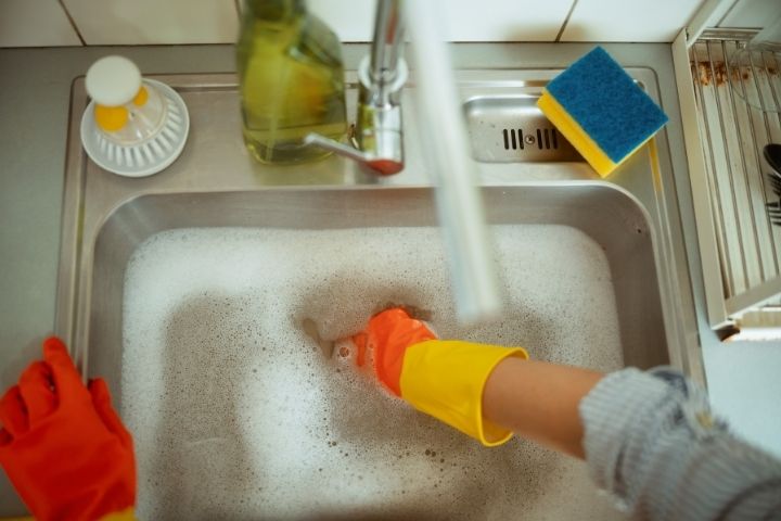 A homeowner in gloves clearing a backed-up sink while learning how to unclog a garbage disposal.