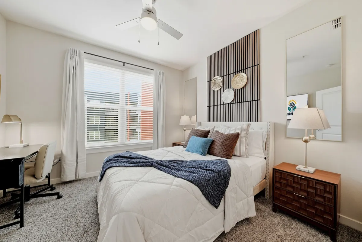Furnished bedroom shown on the SoLiving website, with a blue throw and a desk by the window