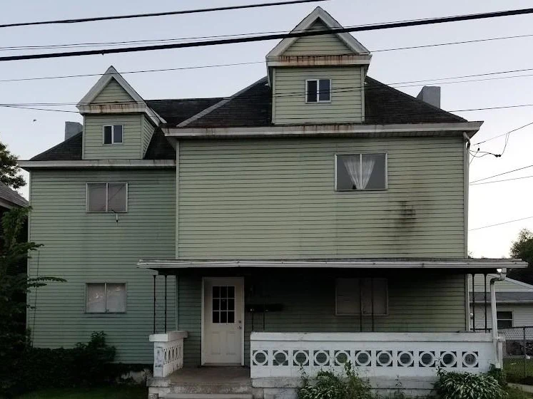Two story home with worn green siding before