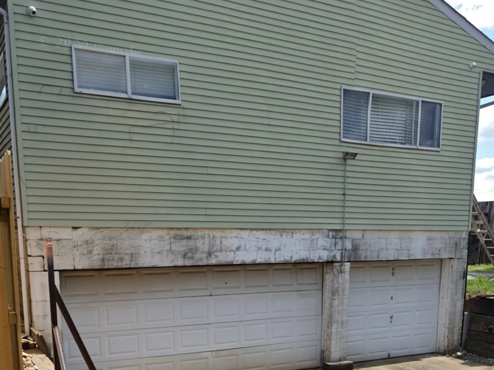 Home with faded green siding and stained garage before