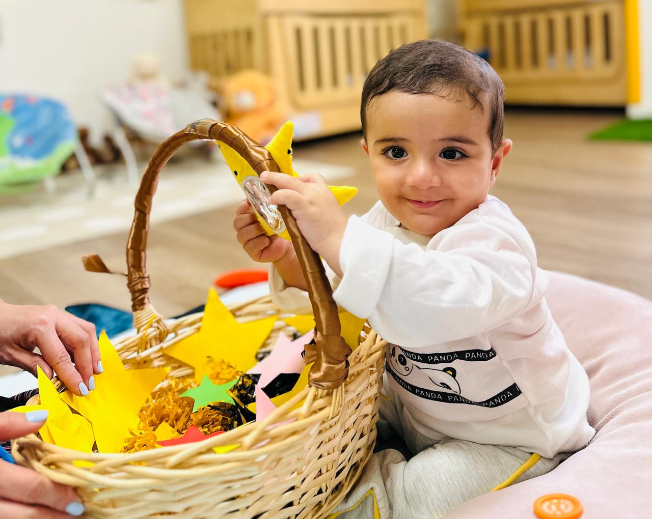 Baby exploring an open-ended sensory basket at Discovery Nursery, touching and investigating colourful materials and objects