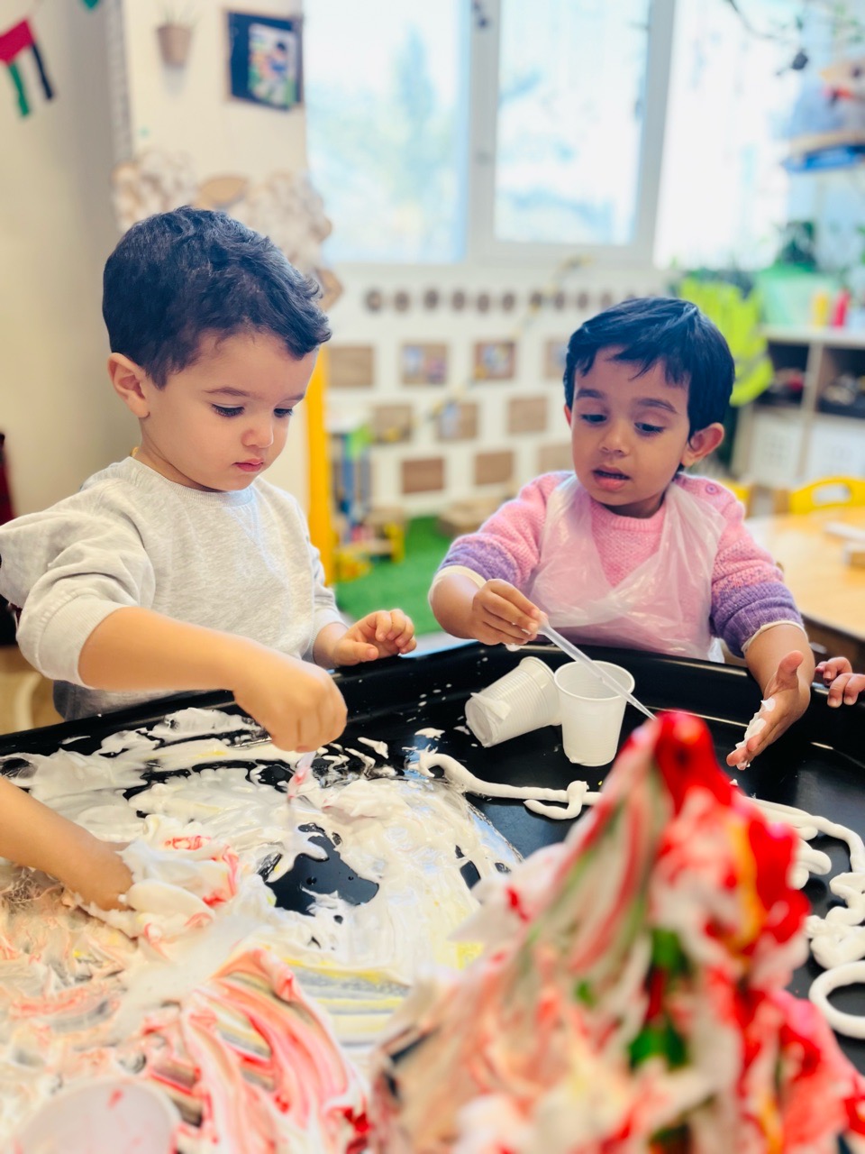 Toddlers exploring a messy sensory activity by scooping, pouring and mixing materials at Discovery Nursery