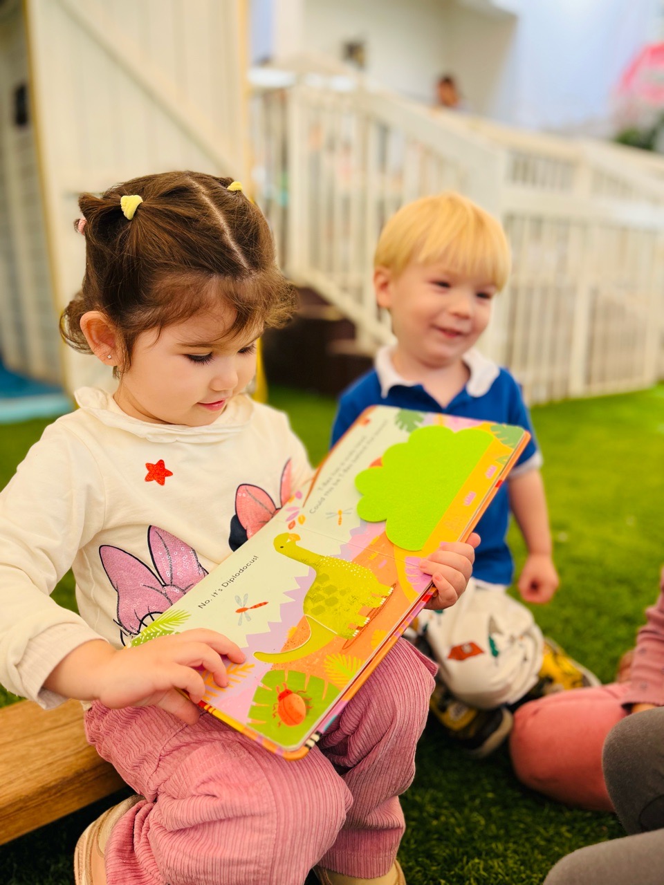 Two children exploring a picture book together at Discovery Nursery, sharing a learning experience that encourages communication, connection and curiosity