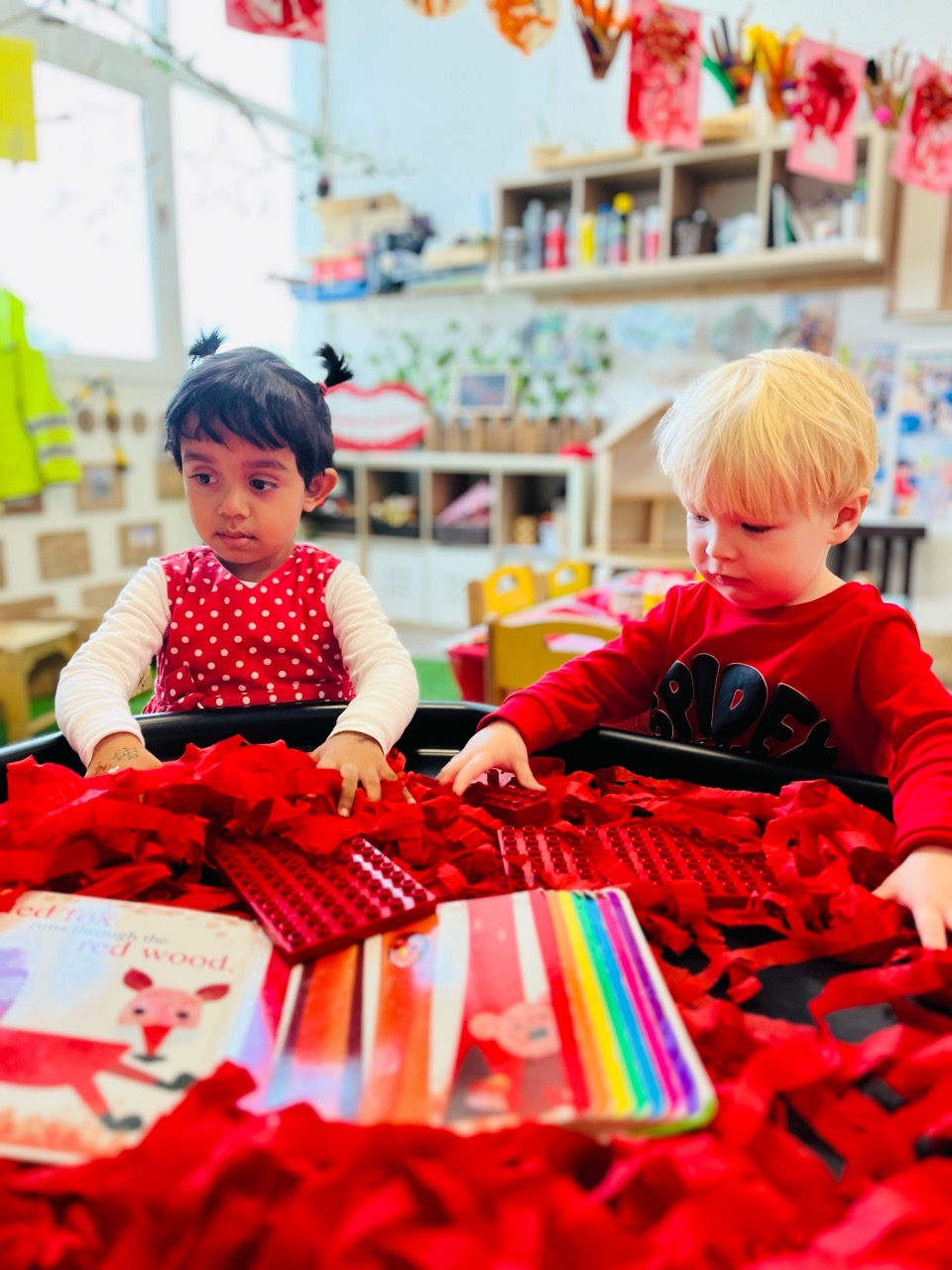 Two preschool children exploring an accessible, thoughtfully arranged sensory and creative play environment at Discovery Nursery, using loose materials and books