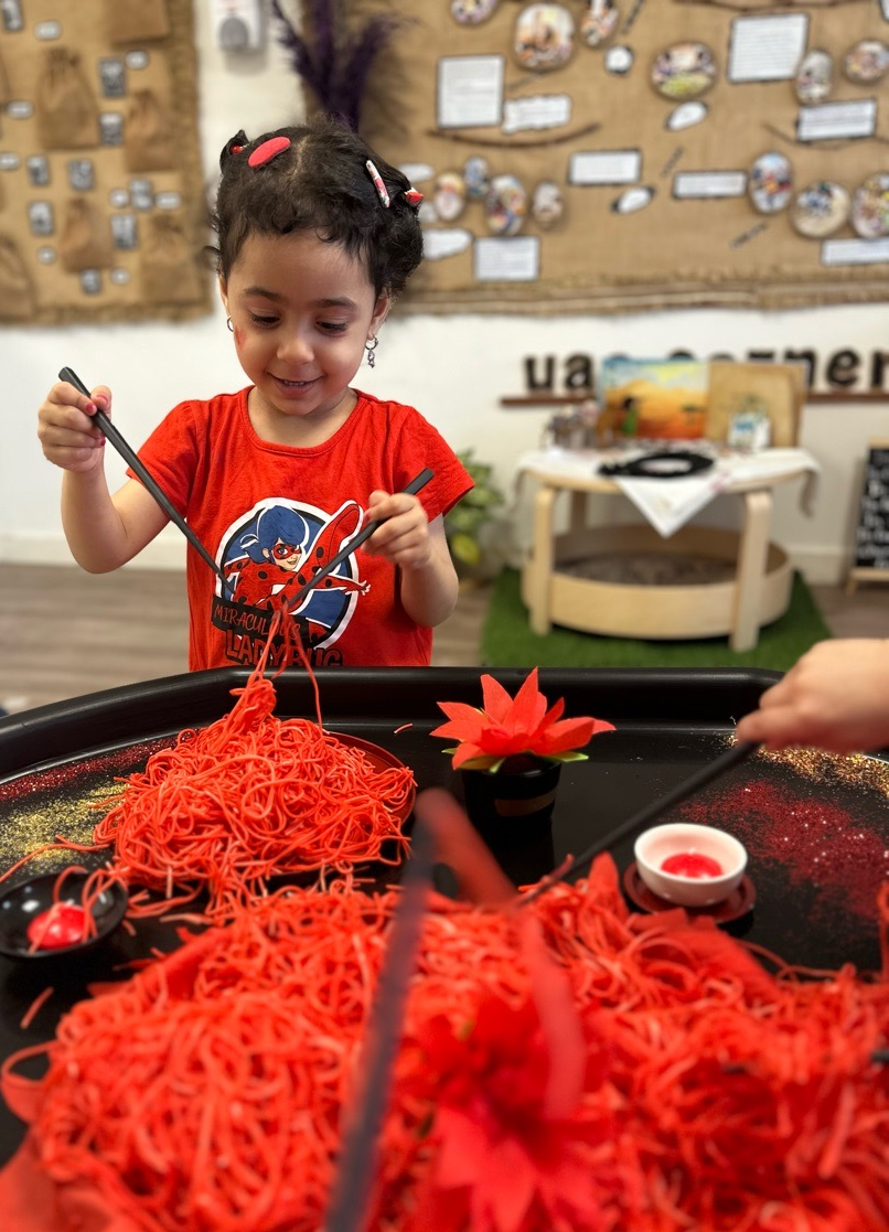 Child exploring an open-ended sensory activity with coloured noodles and loose parts at Discovery Nursery Abu Dhabi, using tools to experiment, create and make choices