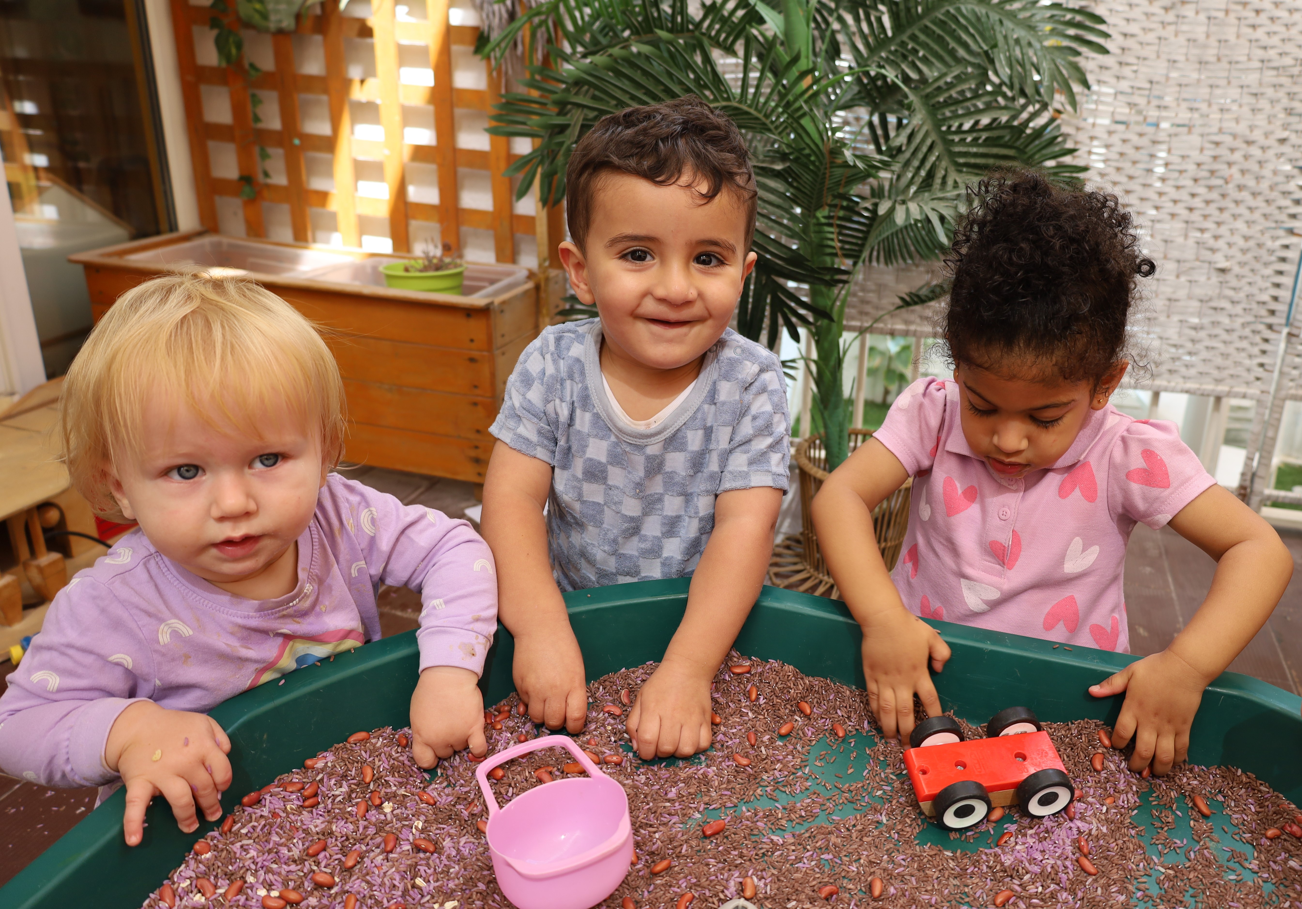Toddlers exploring coloured rice and beans through scooping, filling and sensory play at Discovery Nursery
