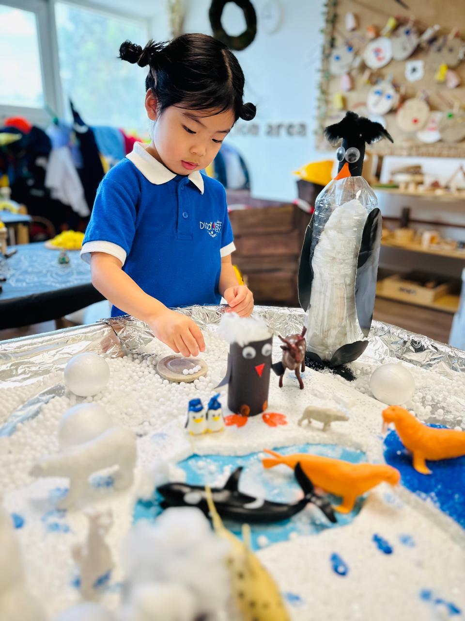 Child exploring a winter-themed sensory play activity at Discovery Nursery using open-ended materials, including cotton, ice-like textures, water and small-world animal figures