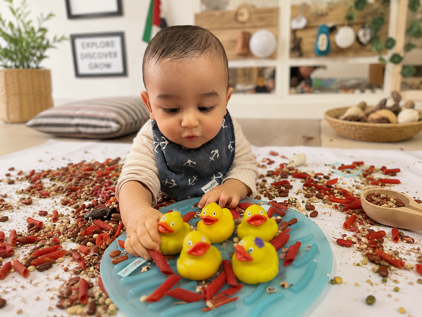 Baby exploring a sensory play activity with textured materials and small yellow duck figures at Discovery Nursery