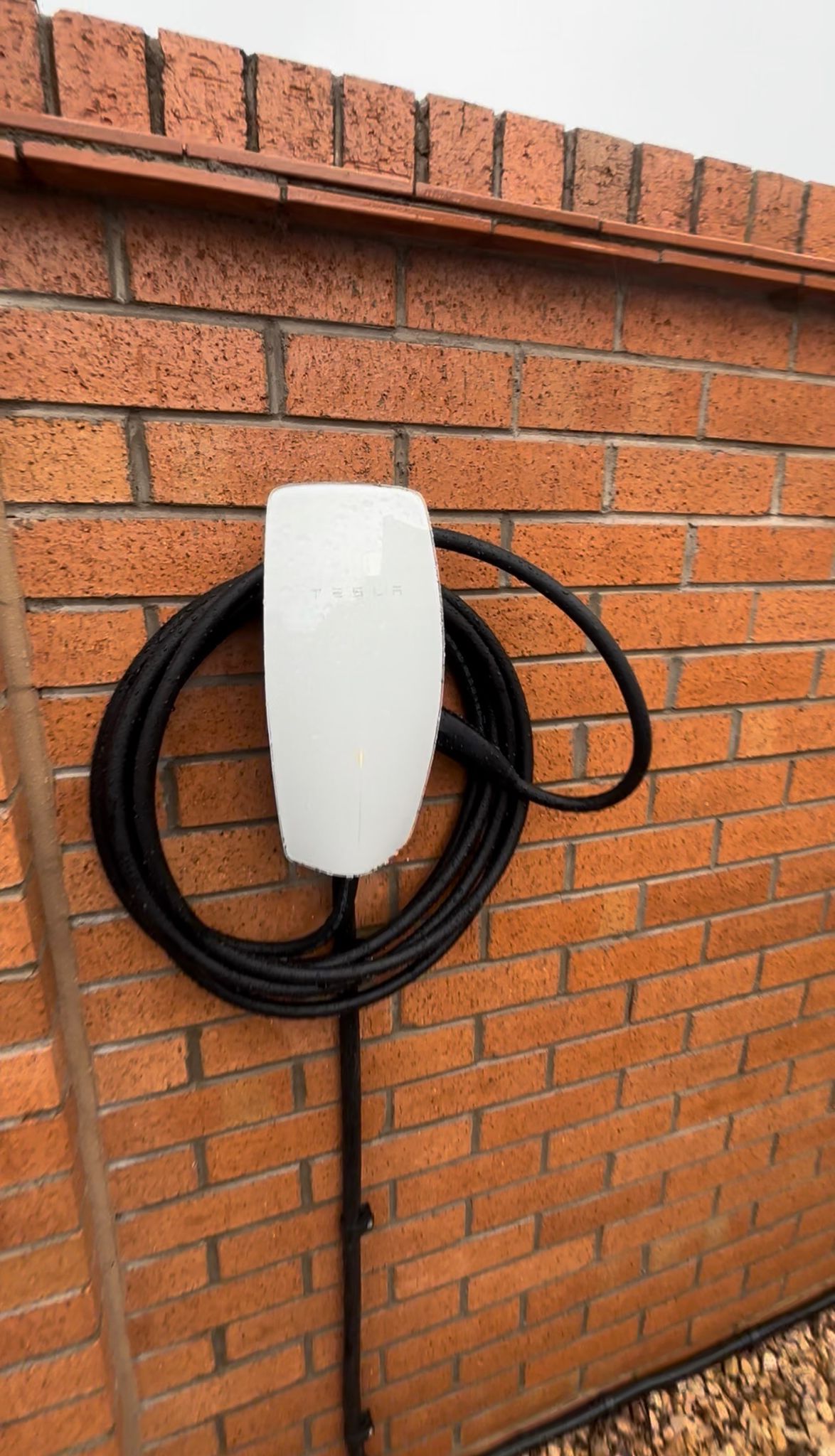 White EV charger installed neatly on an exterior brick wall by Blackline Electrical