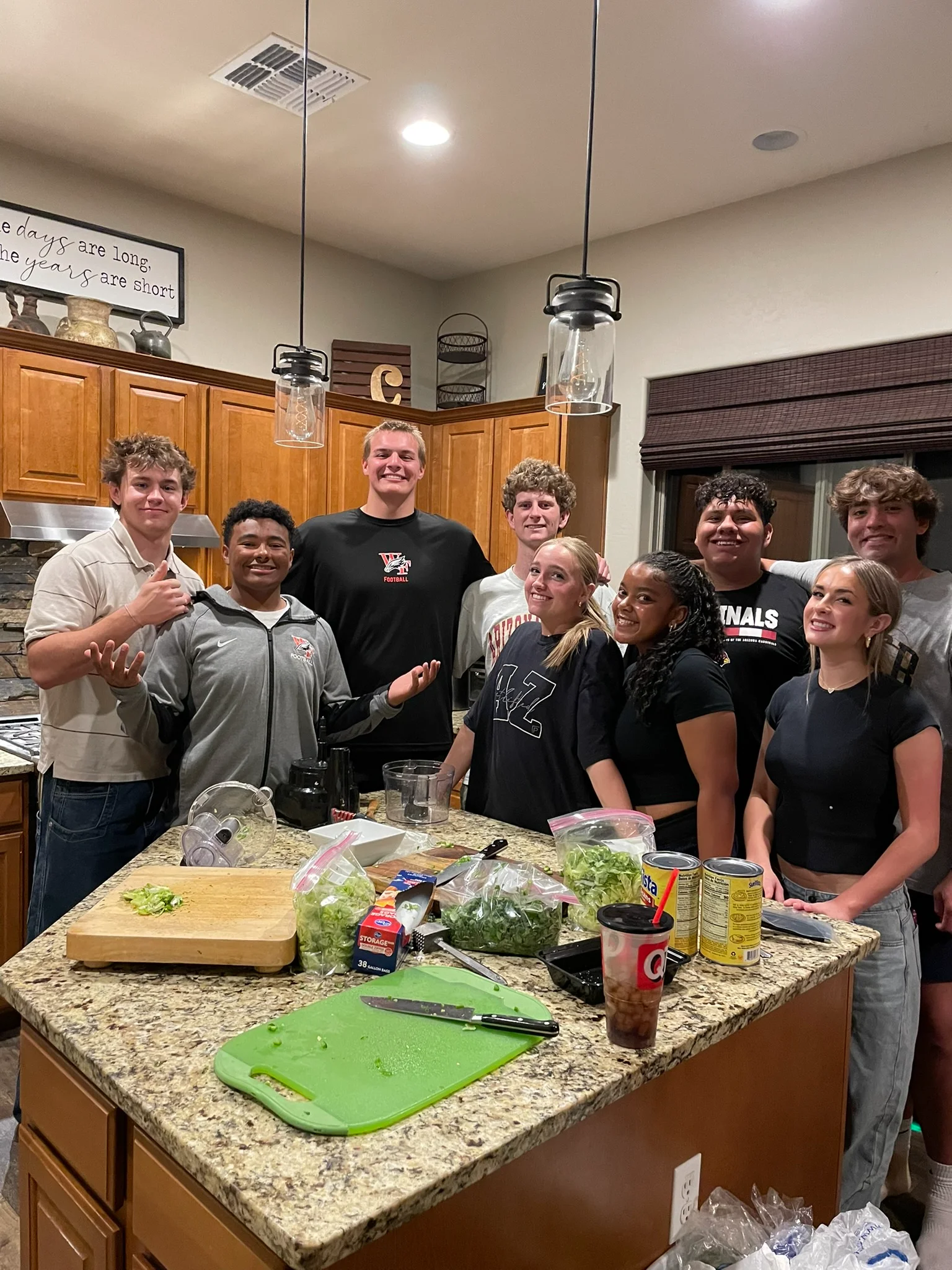 A group of happy young friends gathered in a kitchen, smiling and posing around an island with food preparation.