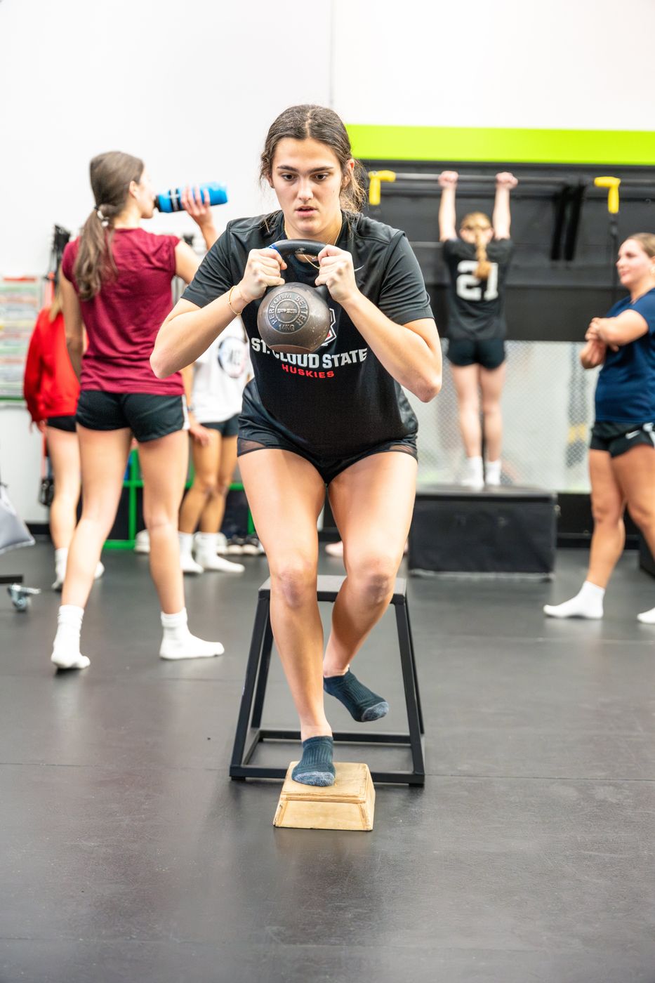 Female athlete doing a single leg box step down holding a kettlebell