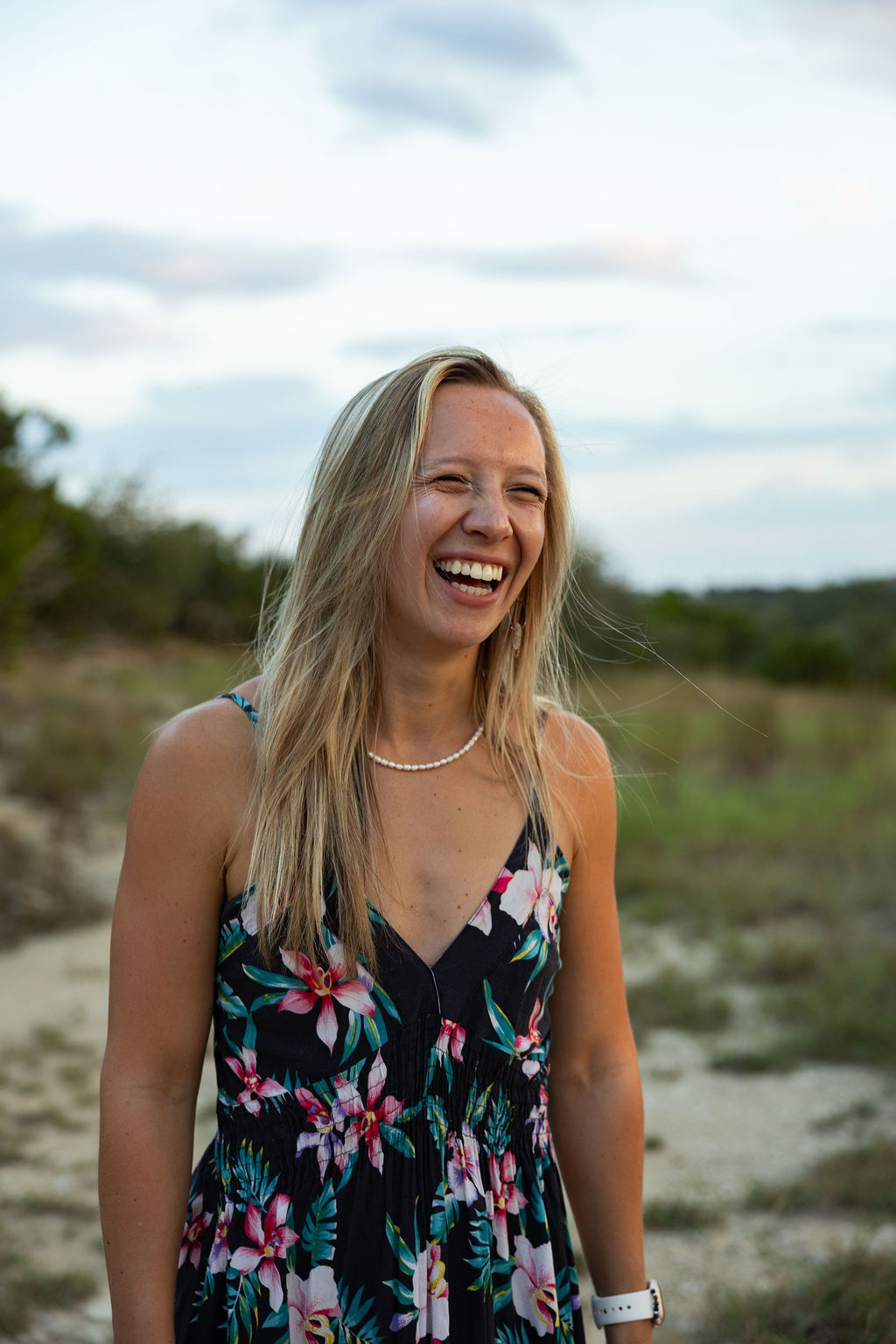 Founder of Aligned and Empowered, Karleigh Lindsay, laughing in nature. She has blonde hair and is wearing a floral dress with a small pearl necklace