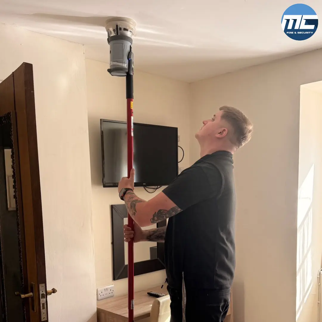 MC Fire & Security engineer testing a smoke detector with SOLO pole — annual BS-5839 service