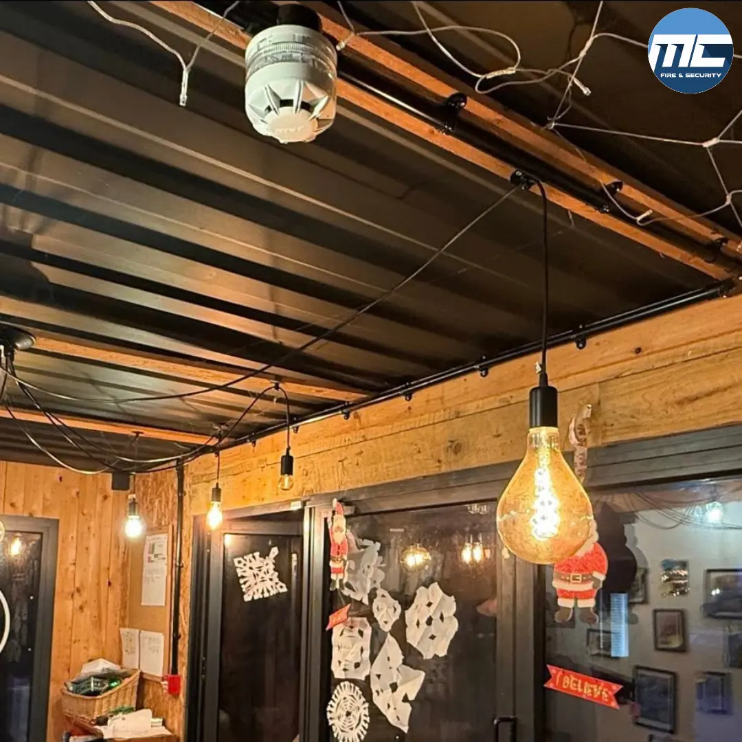 Fire detector on a timber-clad ceiling with Edison-bulb lighting in a children's nursery space